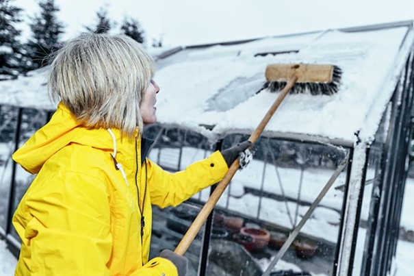 Žena odstraňuje sneh z konštrukcie skleníka